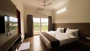 Habitación de hotel con una cama grande, televisión de pantalla plana, ventilador de techo y vistas a zonas verdes por la ventana.