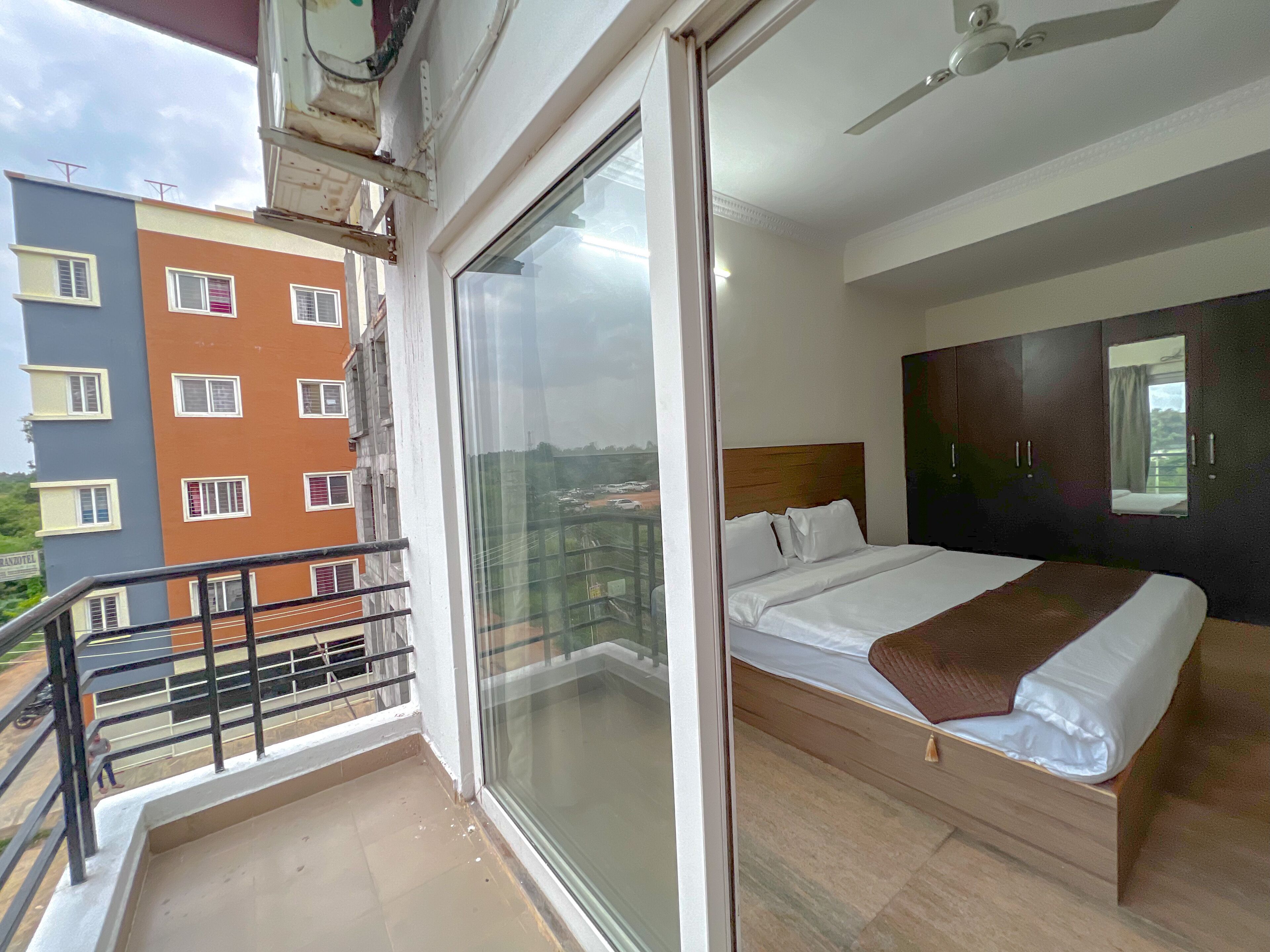 A hotel room with a balcony, a bed with white linens, and a view of the cityscape.