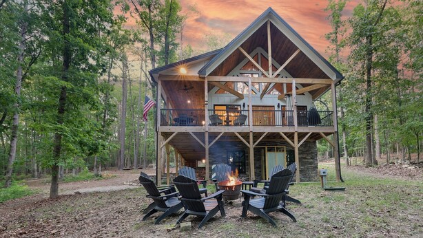 A cabin with a fire pit and outdoor seating, surrounded by trees.