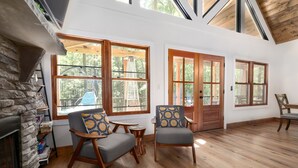 A spacious living area with a stone fireplace, large windows, wooden flooring, and comfortable seating.
