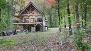 A cabin with a large deck and multiple windows, surrounded by a forest.