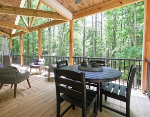 A wooden deck with a table and chairs, surrounded by a railing, overlooking a forest. - Kerr Lake-Pvt Dock included-Beach area and Cove (Manson)
