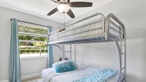 A bunk bed room with a ceiling fan, a window with curtains, and a patterned rug.