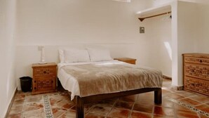 Une chambre à coucher avec un lit, des tables de chevet, une commode en bois et deux fenêtres.