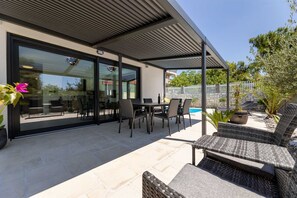 Une terrasse extérieure moderne, dotée d’un espace salon couvert, d’une piscine et d’un mur en pierre.