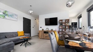 Un salon moderne avec un canapé gris, une table à manger en bois dressée pour six personnes et un téléviseur à écran plat fixé au mur.