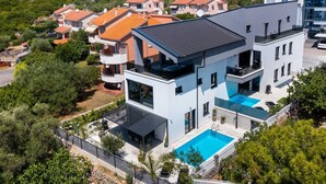 Une maison moderne à deux étages, dotée d’une terrasse sur le toit, d’une piscine et d’un jardin.