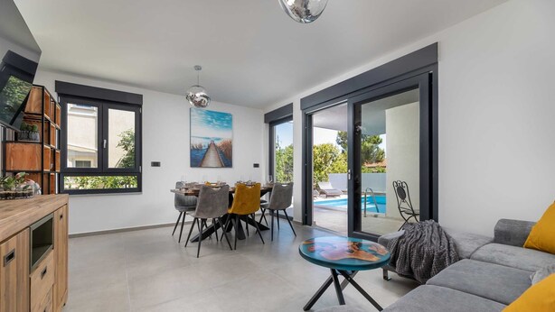 Un salon moderne avec un canapé gris, une table basse en verre et un coin repas comprenant une table et des chaises en bois.