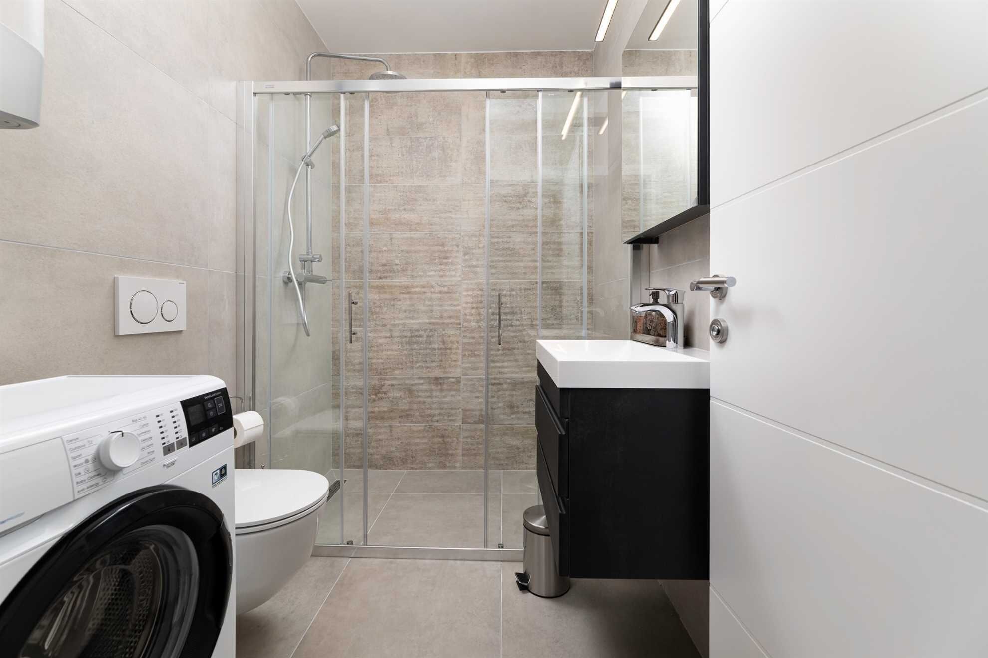 Ein modernes Badezimmer mit einer Duschkabine, einer Waschmaschine, einer Toilette und einem Waschbecken mit schwarzem Unterschrank.
