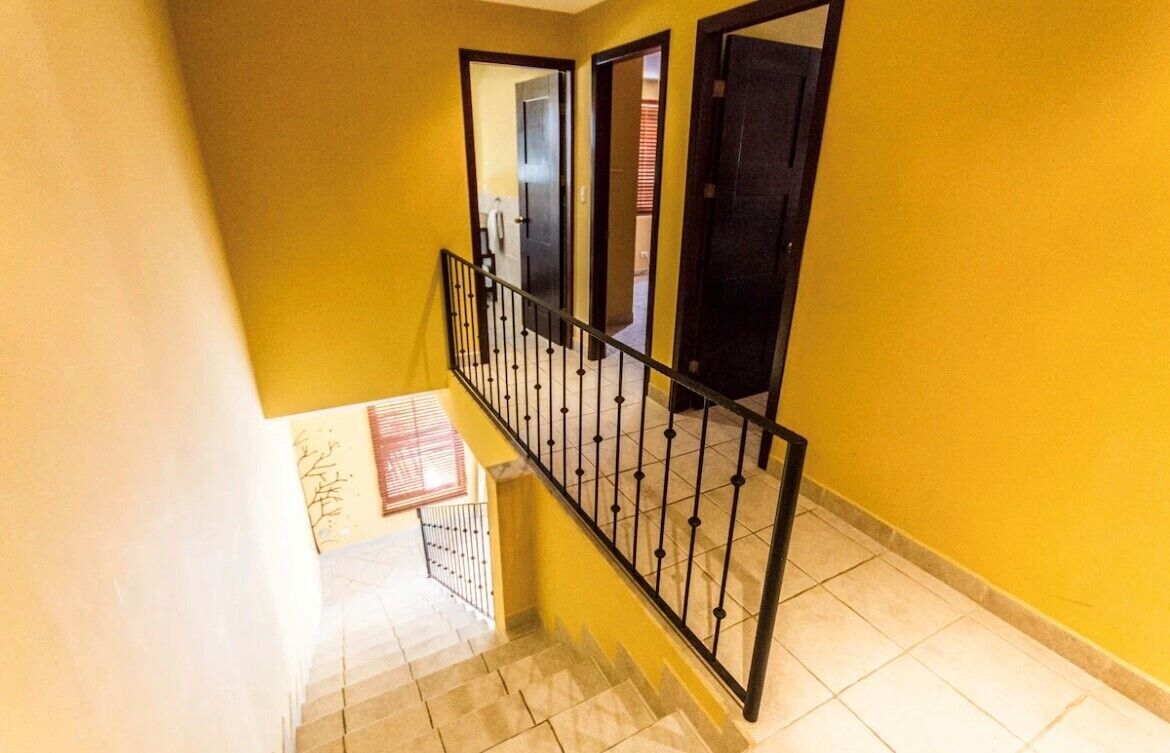 A staircase with a yellow wall and black railing leading to an upper floor.