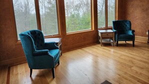 Una habitación con ventanas amplias, un sillón azul, una mesita y una silla a juego.