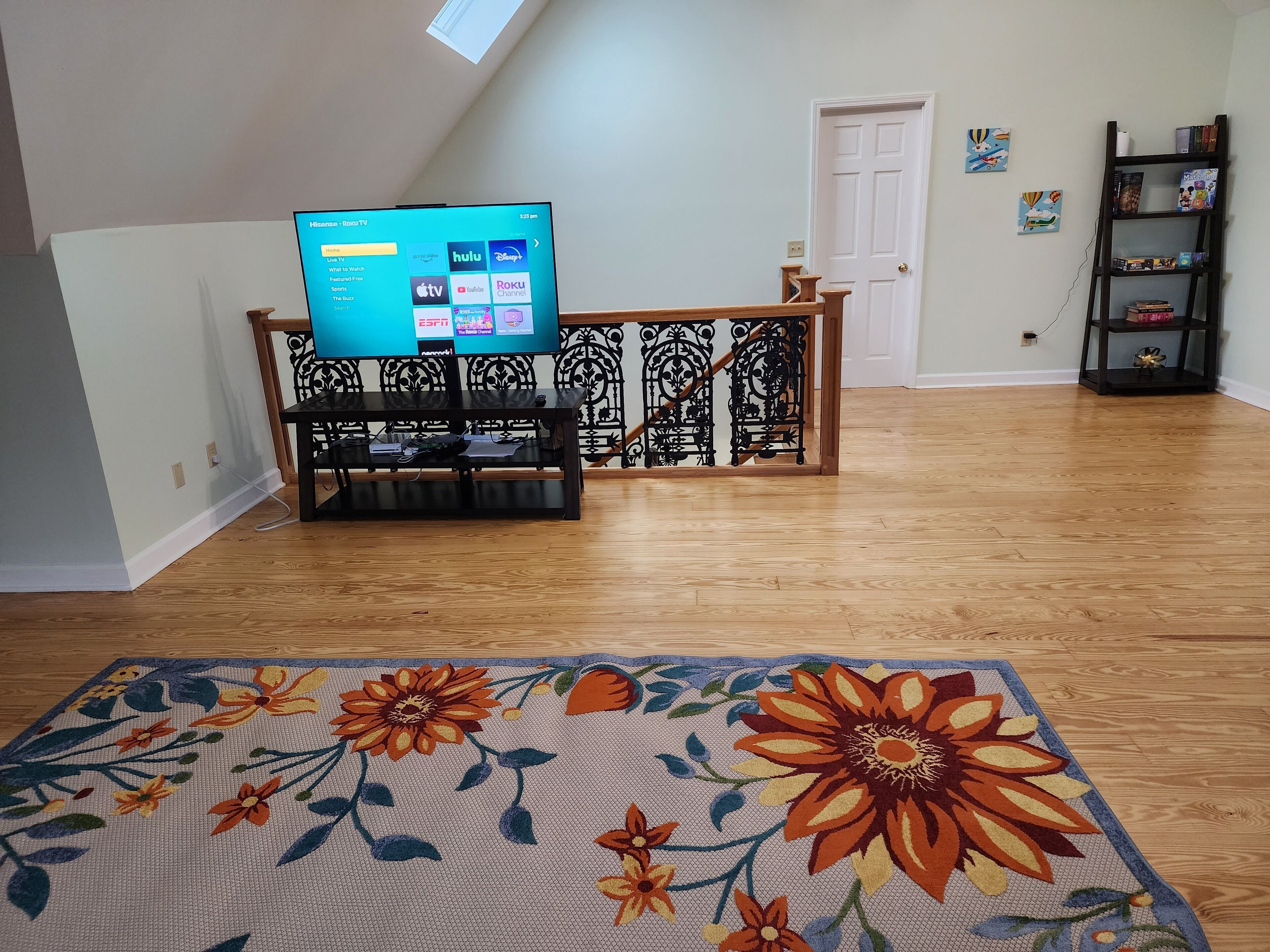 Ein Wohnzimmer mit Fernseher auf einem Schrank, einem floralen Teppich, einem Bücherregal und einer Tür.