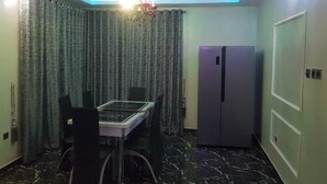Une pièce de taille modeste comprenant une table et des chaises, un réfrigérateur et un rideau.