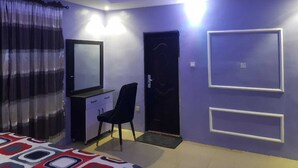 Une pièce comprenant un lit, un bureau avec une chaise, une porte et deux tableaux encadrés accrochés au mur.