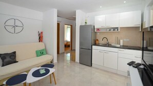 A compact living space with a kitchenette, a sofa with cushions, a small table, and a clock on the wall. - Holiday Home Eta with Pool (Rovinj)