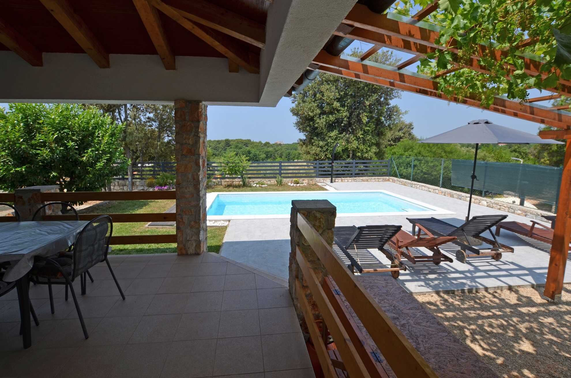 A covered patio area with a pool, outdoor furniture, and a view of the surrounding landscape.