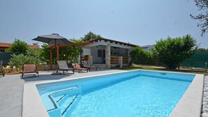 A swimming pool with lounge chairs and an umbrella, surrounded by a house and greenery. - Holiday Home Eta with Pool (Rovinj)