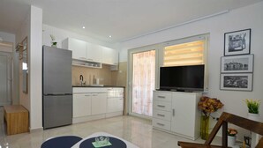 A modern kitchen with white cabinets, a built-in oven, and a flat-screen TV. There is a dining area with a table and chairs, and a small wooden bench. - Holiday Home Eta with Pool (Rovinj)