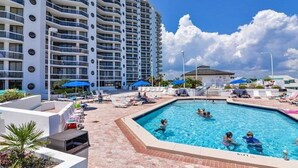 A hotel pool area with a large pool, lounge chairs, and umbrellas.