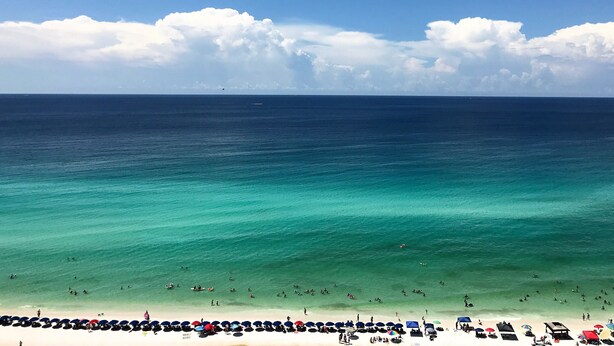 A beach with clear turquoise waters, a sandy shore, and a line of umbrellas.