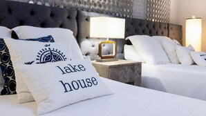 A hotel room with a tufted headboard, a nightstand with a lamp, and a bed with white bedding and decorative pillows. - Private Room #3 (Seneca)