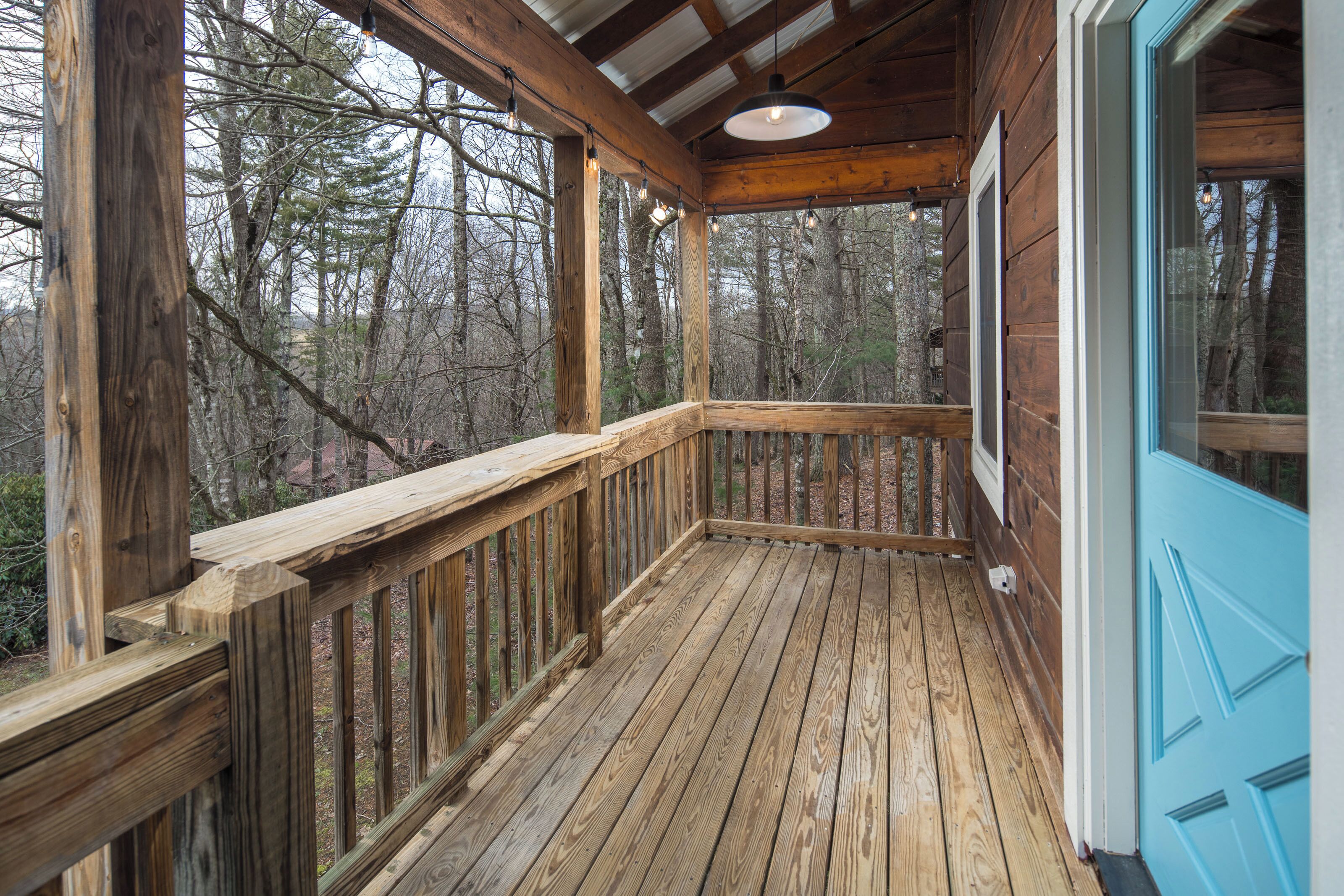 A wooden deck with a blue door, surrounded by trees.
