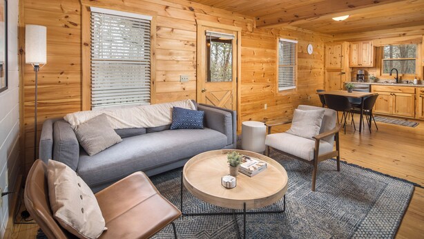 A cozy cabin interior with a sofa, chairs, a coffee table, and a kitchen area.
