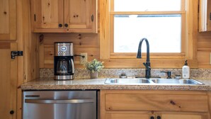 A kitchen with wooden cabinets, a stainless steel dishwasher, a coffee maker, a sink, and a window above the sink.