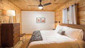 A wooden-paneled bedroom with a bed, a dresser, a ceiling fan, and two framed pictures on the wall.