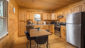 A wooden cabin kitchen with a dining table, chairs, a refrigerator, and a stove.