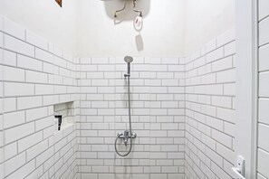 A bathroom with white tiled walls and a shower with a handheld showerhead.