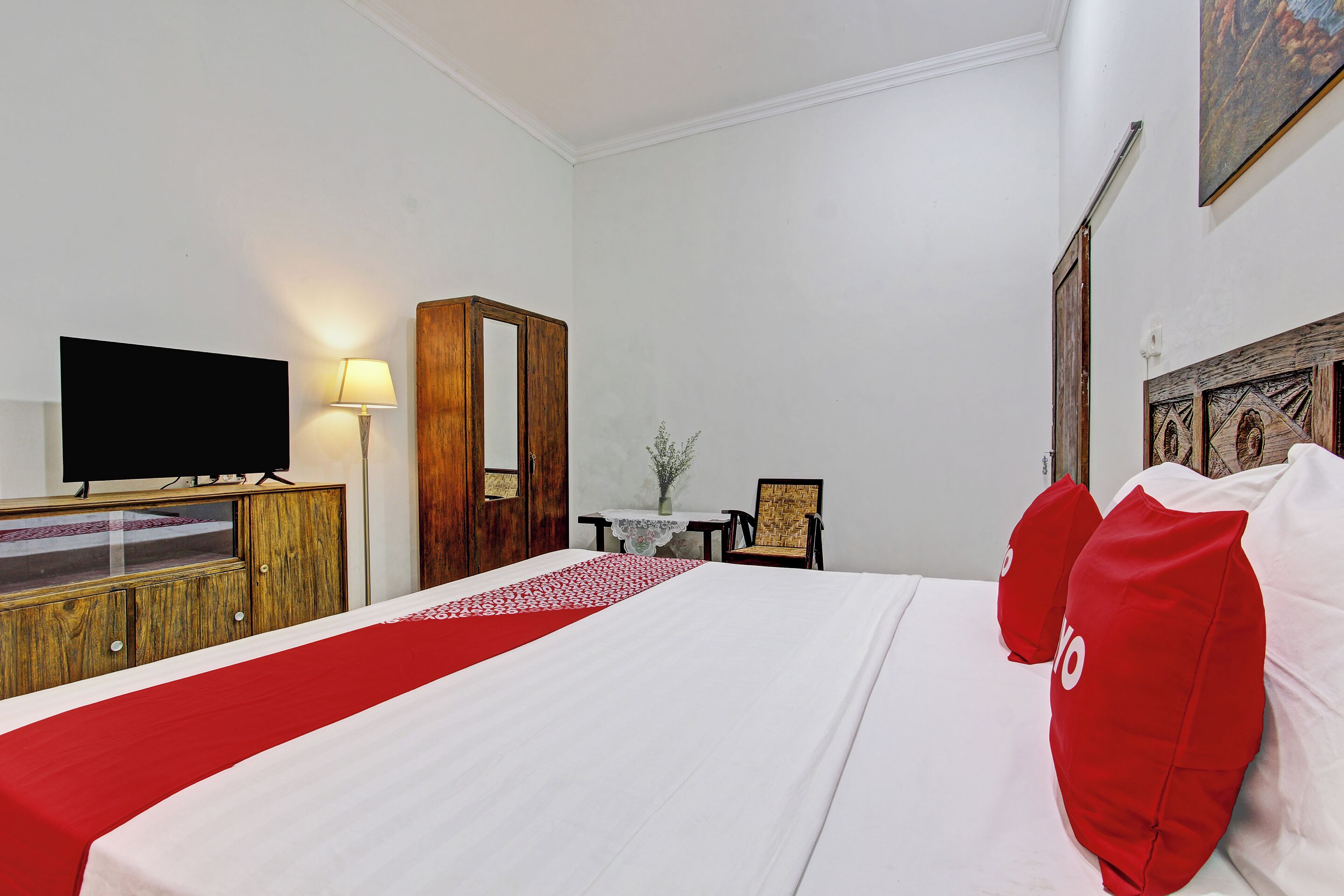 Ein Hotelzimmer mit einem großen Bett, einem Fernseher, einer Holzkabine, einem kleinen Tisch mit einer Vase und einem Sessel.