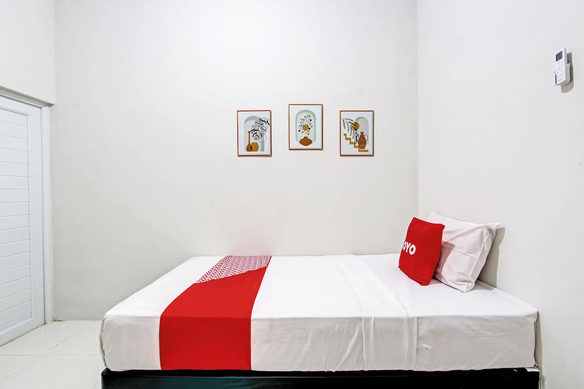 Ein Schlafzimmer mit einem Bett, einem roten Kopfkissen und drei gerahmten Bildern an der Wand.