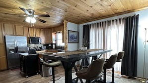 Una cucina rustica con mobili in legno, un frigorifero in acciaio inossidabile, un forno a microonde e un piano cottura. C'è un'area pranzo con un tavolo e quattro sedie.