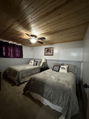 A bedroom with two beds, a ceiling fan, a nightstand, and a window with curtains.