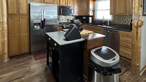 Una cucina con mobili in legno, un frigorifero in acciaio inossidabile, un forno a microonde, un lavello e una ventola a soffitto.
