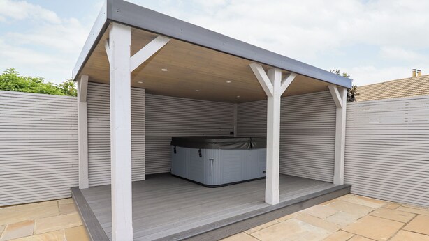 Un patio coperto con vasca idromassaggio, travi in legno bianco e pavimento in pietra.