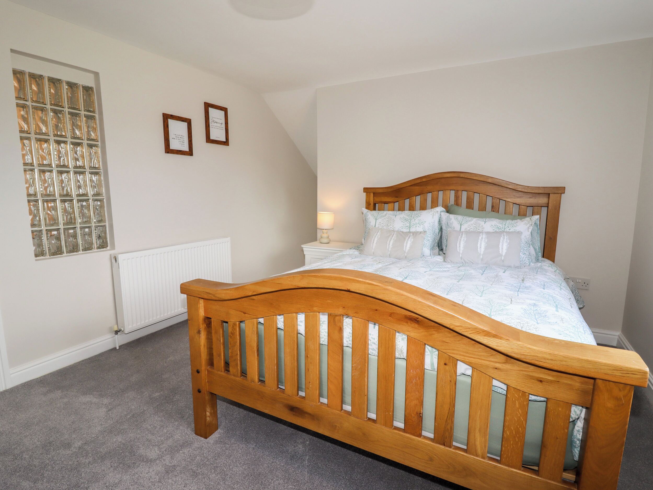 A bedroom with a wooden bed, a radiator, a window with frosted glass, and two framed pictures on the wall.