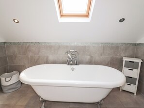 A bathroom with a freestanding bathtub, a small white cabinet, and a skylight above. - 4 Bodnant Road (Colwyn Bay)
