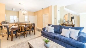A spacious living room with a blue sofa, dining table, and chairs. There is a chandelier and a large mirror on the wall. - Charming 3BR Townhome in Kissimmee, perfect for family getaways! (Kissimmee)