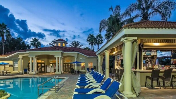 A poolside area with lounge chairs, a bar, and a building with a red-tiled roof. - Charming 3BR Townhome in Kissimmee, perfect for family getaways! (Kissimmee)
