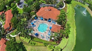 An aerial view of a resort with a central swimming pool, multiple lounge areas, and a surrounding water body. - Charming 3BR Townhome in Kissimmee, perfect for family getaways! (Kissimmee)