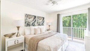 A bedroom with a large bed, two bedside tables, a ceiling fan, and a view of greenery through the window. - Charming 3BR Townhome in Kissimmee, perfect for family getaways! (Kissimmee)