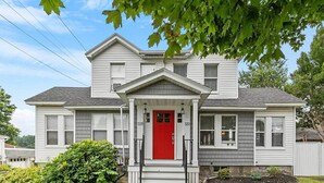A two-story house with a red front door, white trim, and a small porch.