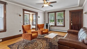 A spacious living room with a ceiling fan, large windows, and a brown leather sofa.