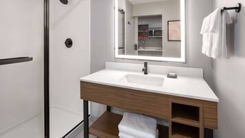 Un baño moderno con cabina de ducha de vidrio, un lavamanos blanco con tocador de madera y un espejo grande sobre el lavamanos.