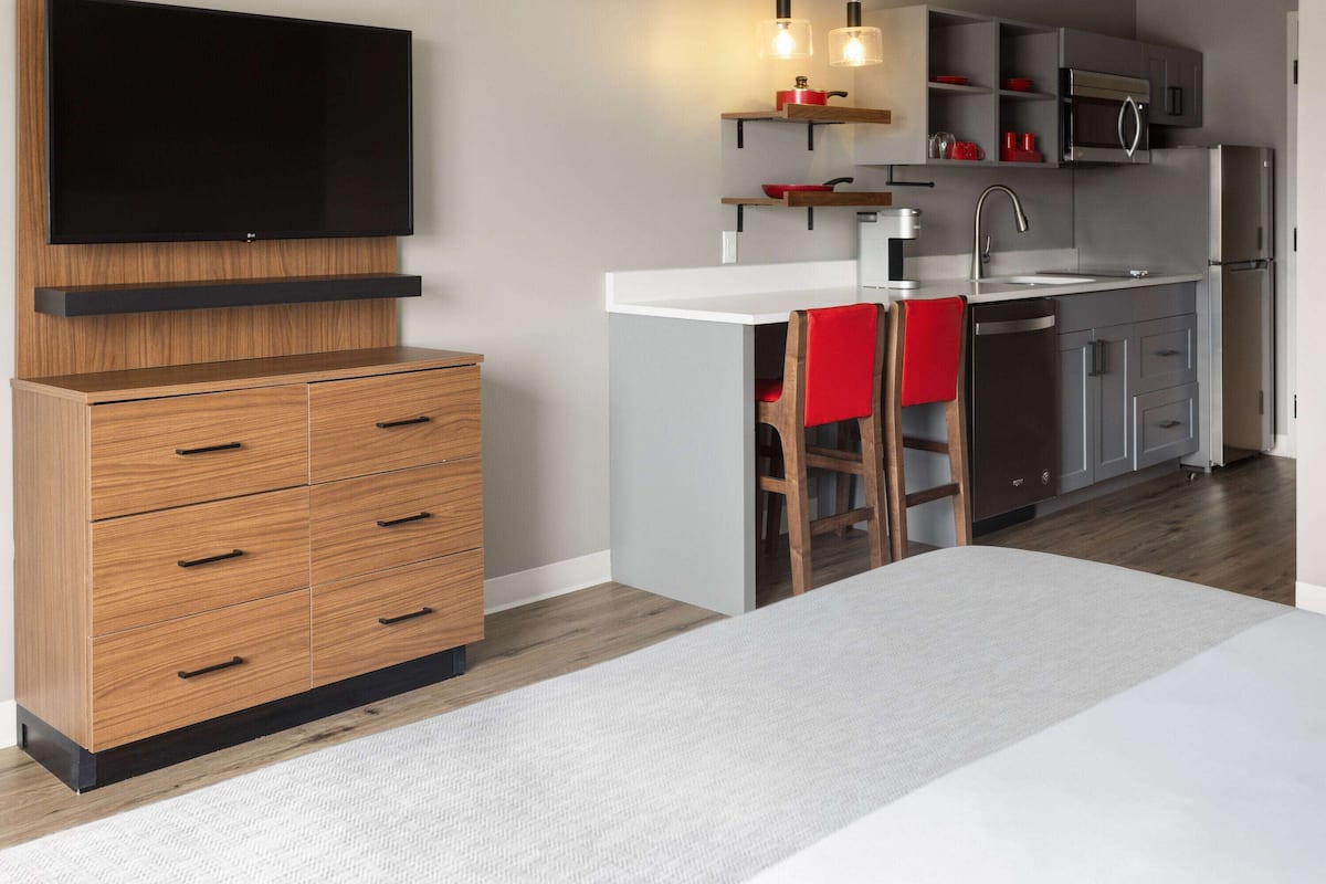 Une cuisine moderne dotée d’un téléviseur à écran plat, de meubles en bois, d’un plan de travail blanc et d’une chaise rouge.