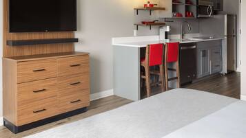 Una cocina moderna con televisor de pantalla plana, armarios de madera, encimera blanca y una silla roja.