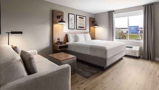 Une chambre d’hôtel moderne équipée d’un lit, d’un canapé, d’une table de chevet et d’une fenêtre avec des rideaux.