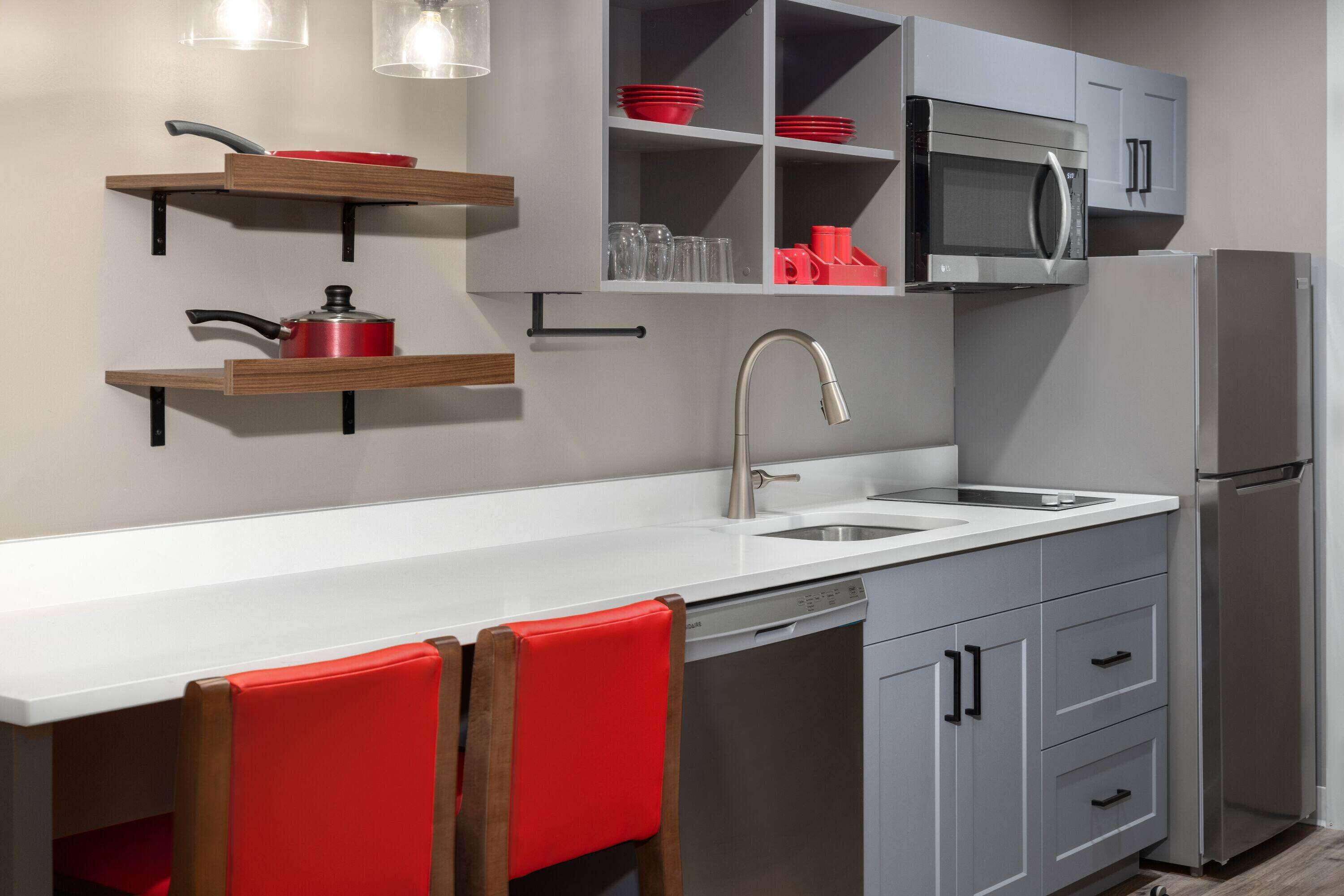 A modern kitchen with a white countertop, stainless steel appliances, and red chairs.